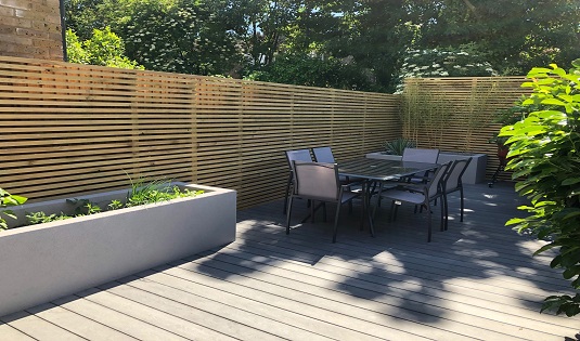 Grey composite decking with horizontal slatted fencing and raised rendered beds, East London